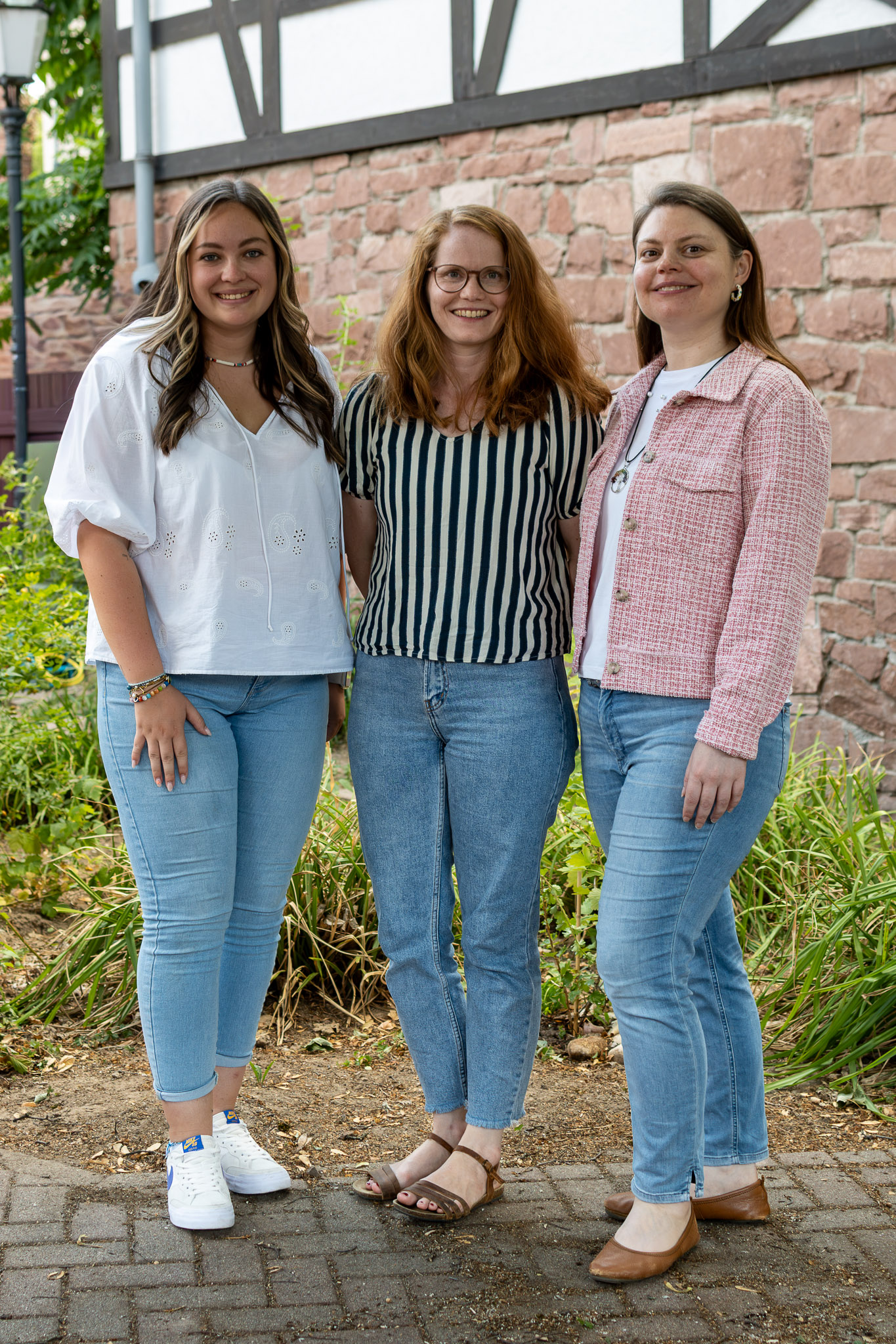 Teamfoto von drei Frauen. Sie stehen nebeneinander in einem Garten. Alle tragen Jeans.